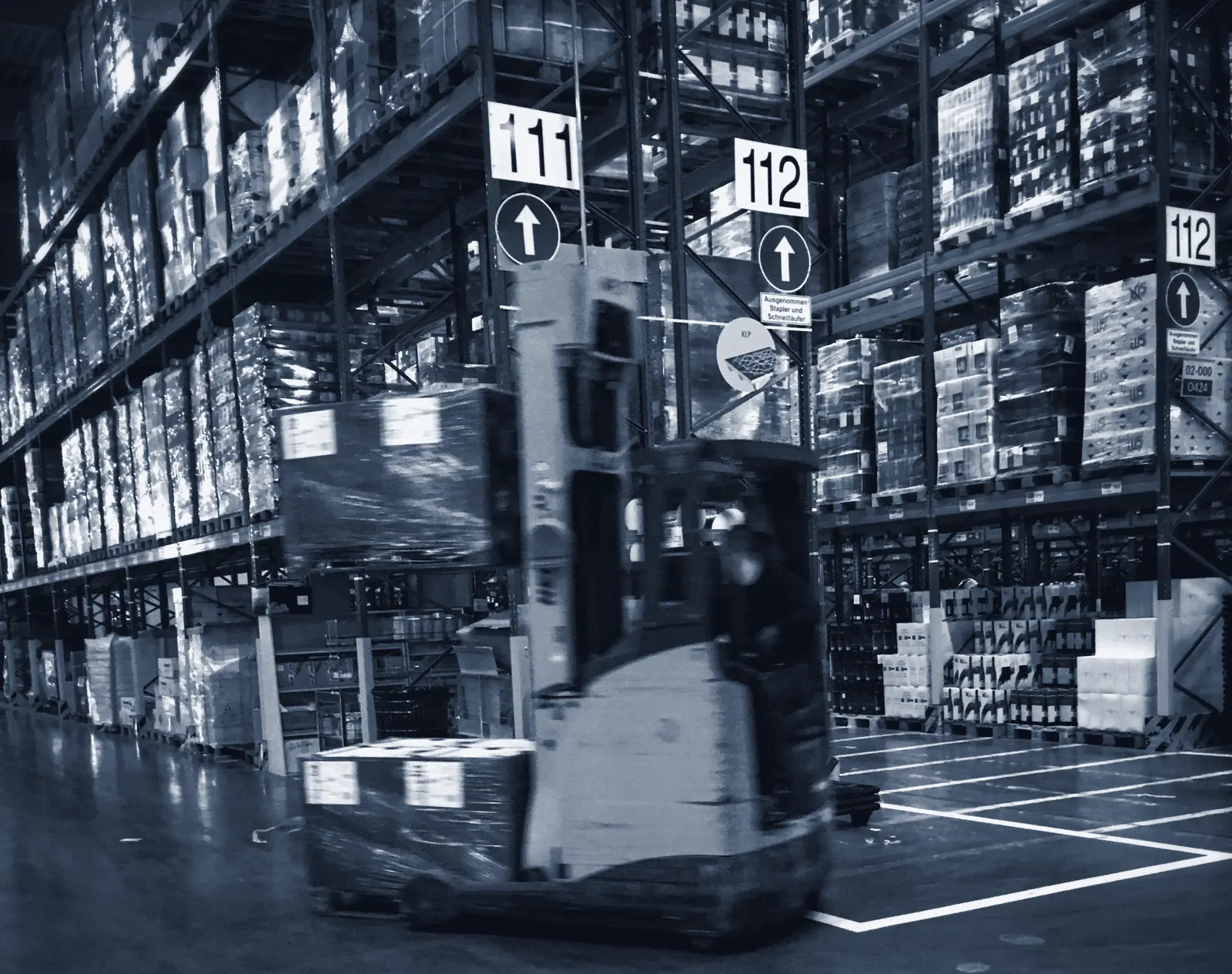 Forklift moving palletised goods through a high-bay warehouse aisle